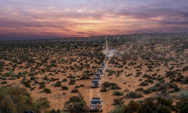 drone shot of expedition vehicles in a convoy driving dusty tracks